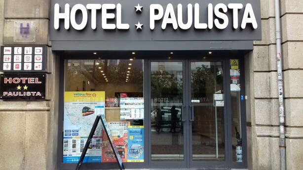 Fachada del Hotel Paulista con un cartel que muestra servicios y un mapa para visitas guiadas por la ciudad.