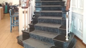 Una imponente escalera con escalones oscuros y barandilla de madera, que conduce a un rellano con pared blanca y molduras decorativas.