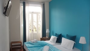 Un dormitorio con una cama, dos mesitas de noche, una ventana con cortinas y vistas a árboles.