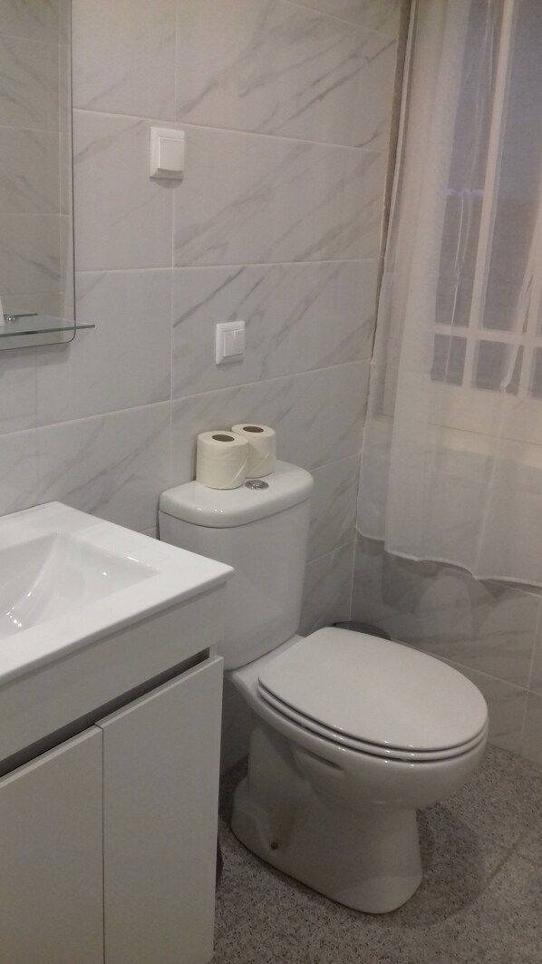 Un baño con lavamanos blanco, inodoro y paredes de mármol.