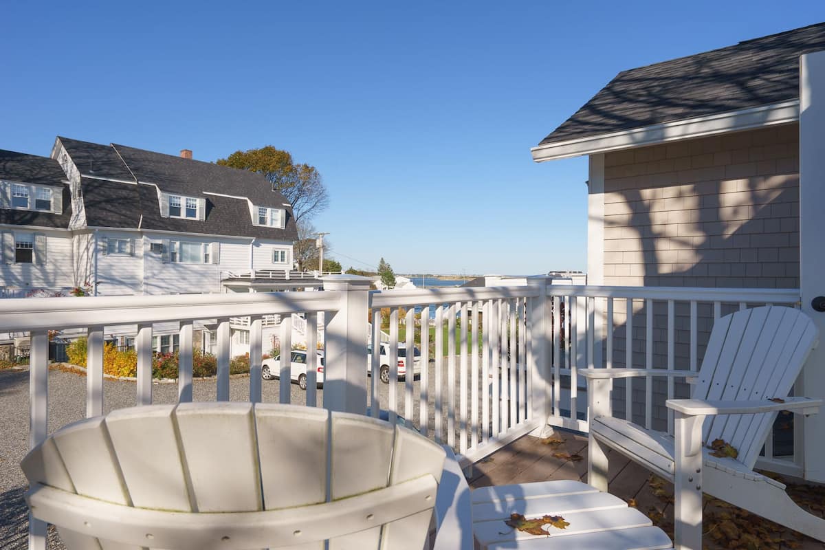 A white deck with a white Adirondack chair and a white Adirondack chair with a white cushion.