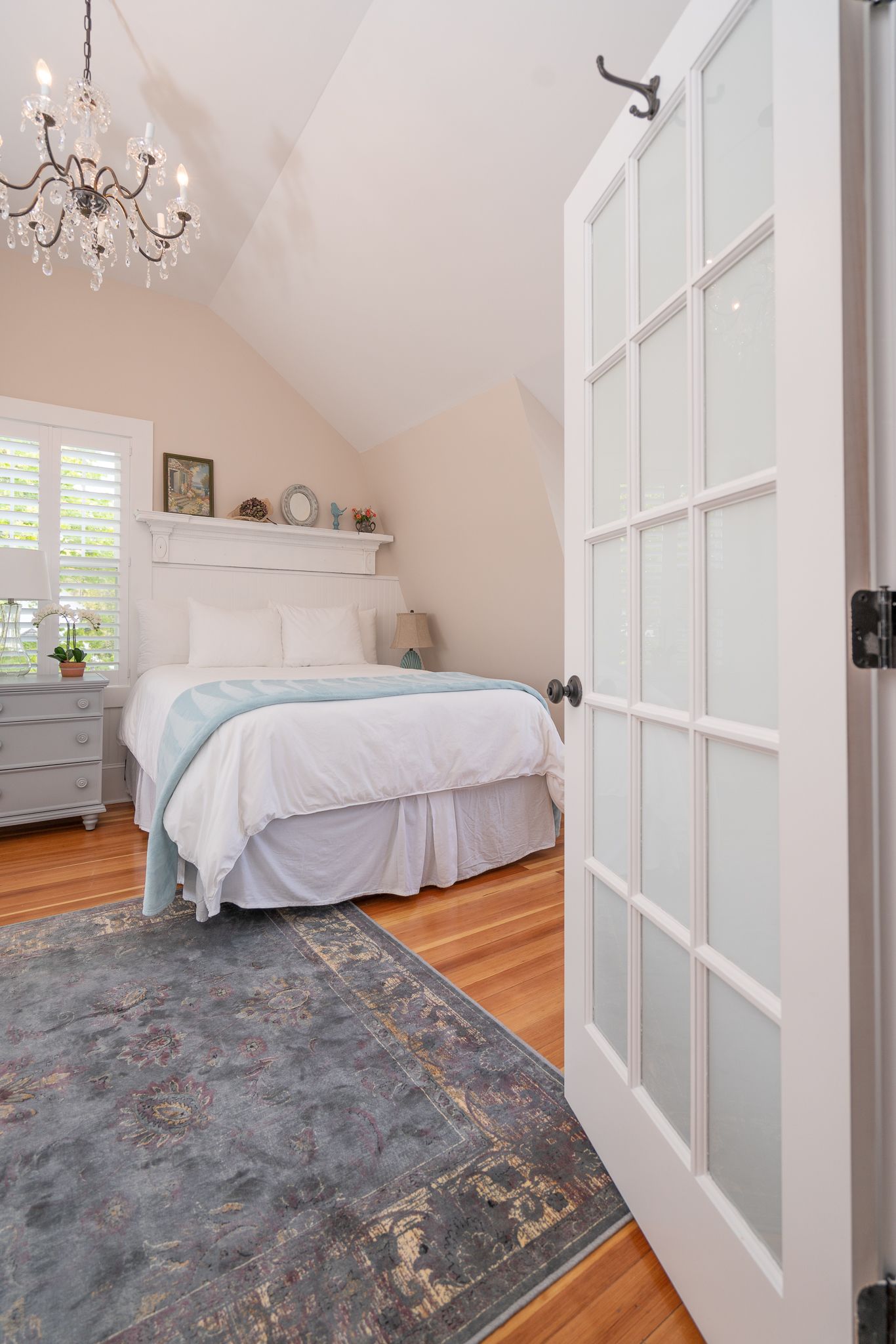 Un dormitorio con cama, cómoda, lámpara de araña, ventana y puerta.
