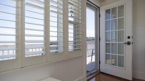 A room with a white bench, a sliding glass door, and a view of a balcony.