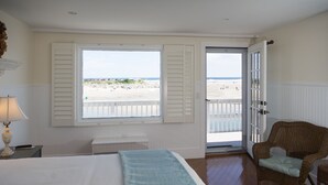 A bedroom with a bed, a chair, a lamp, and a view of the beach through a door.