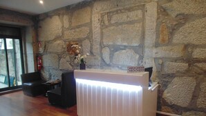 A reception area with a stone wall, a reception desk, a fire extinguisher, a potted plant, and a black leather chair. - Hotel Porto Rico (Porto)