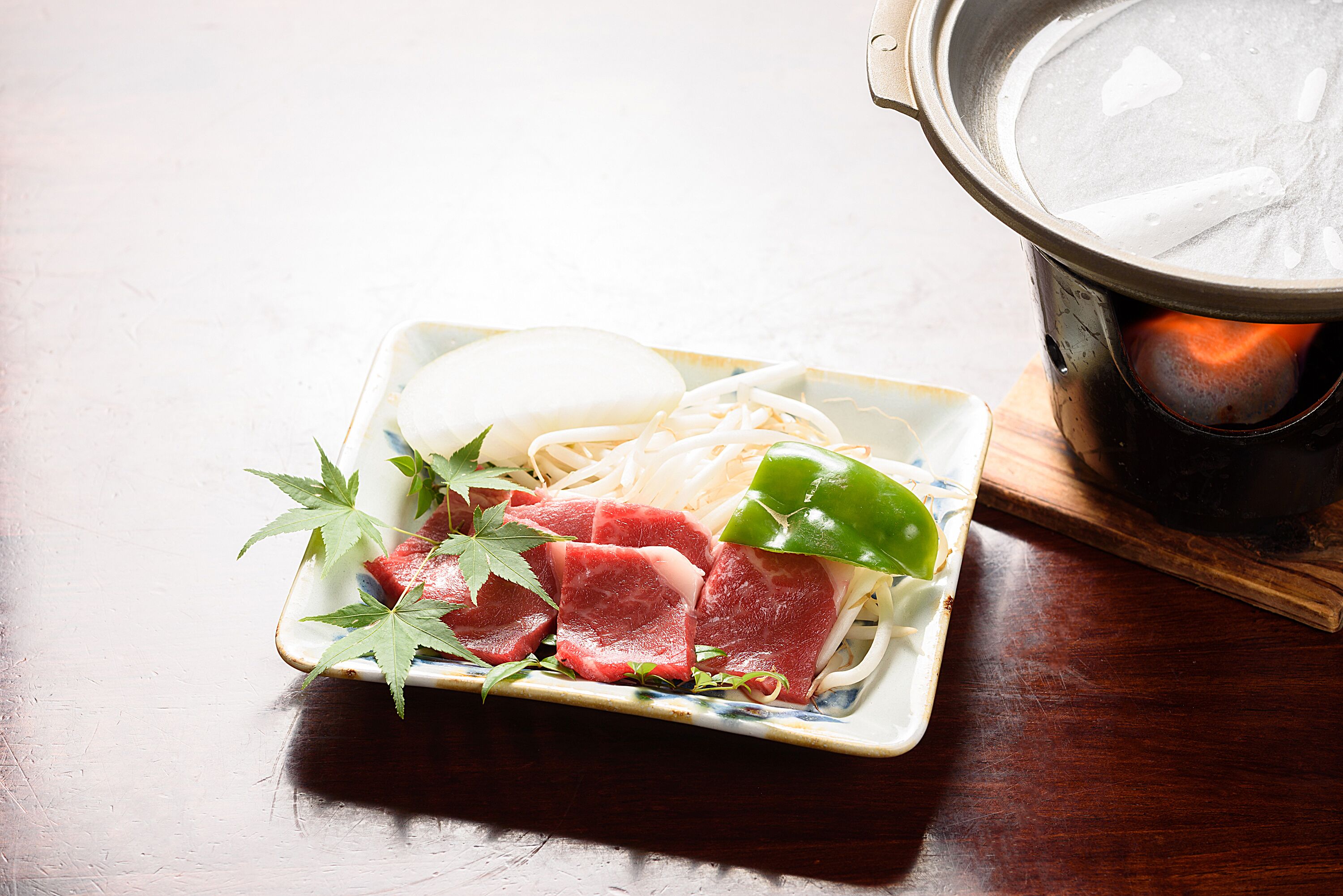 A dish with raw meat, vegetables, and noodles on a ceramic plate.