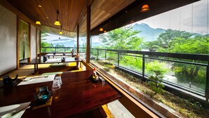 Un restaurante con mesas y sillas de madera, grandes ventanales con vistas a zonas verdes y montañas.