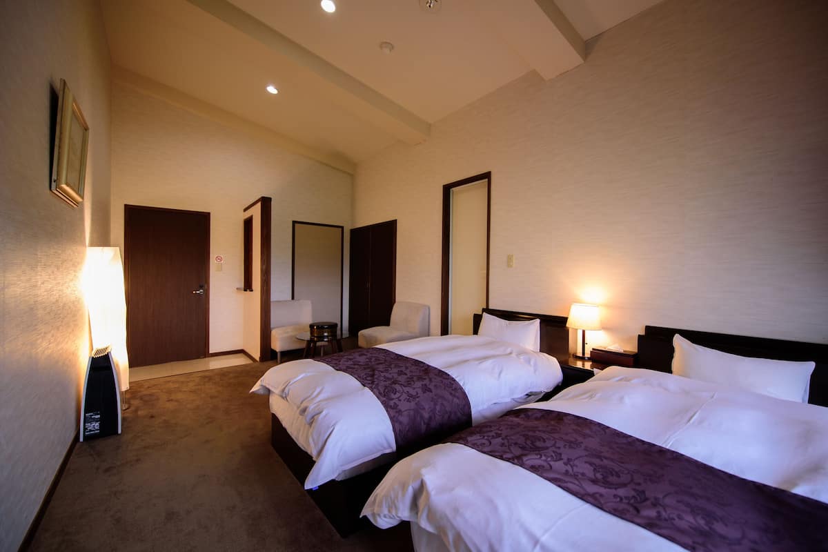 A hotel room with two beds, a sitting area with a chair, a small table, and a mirror.