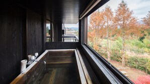 Una bañera de madera con vista a árboles otoñales a través de una ventana.