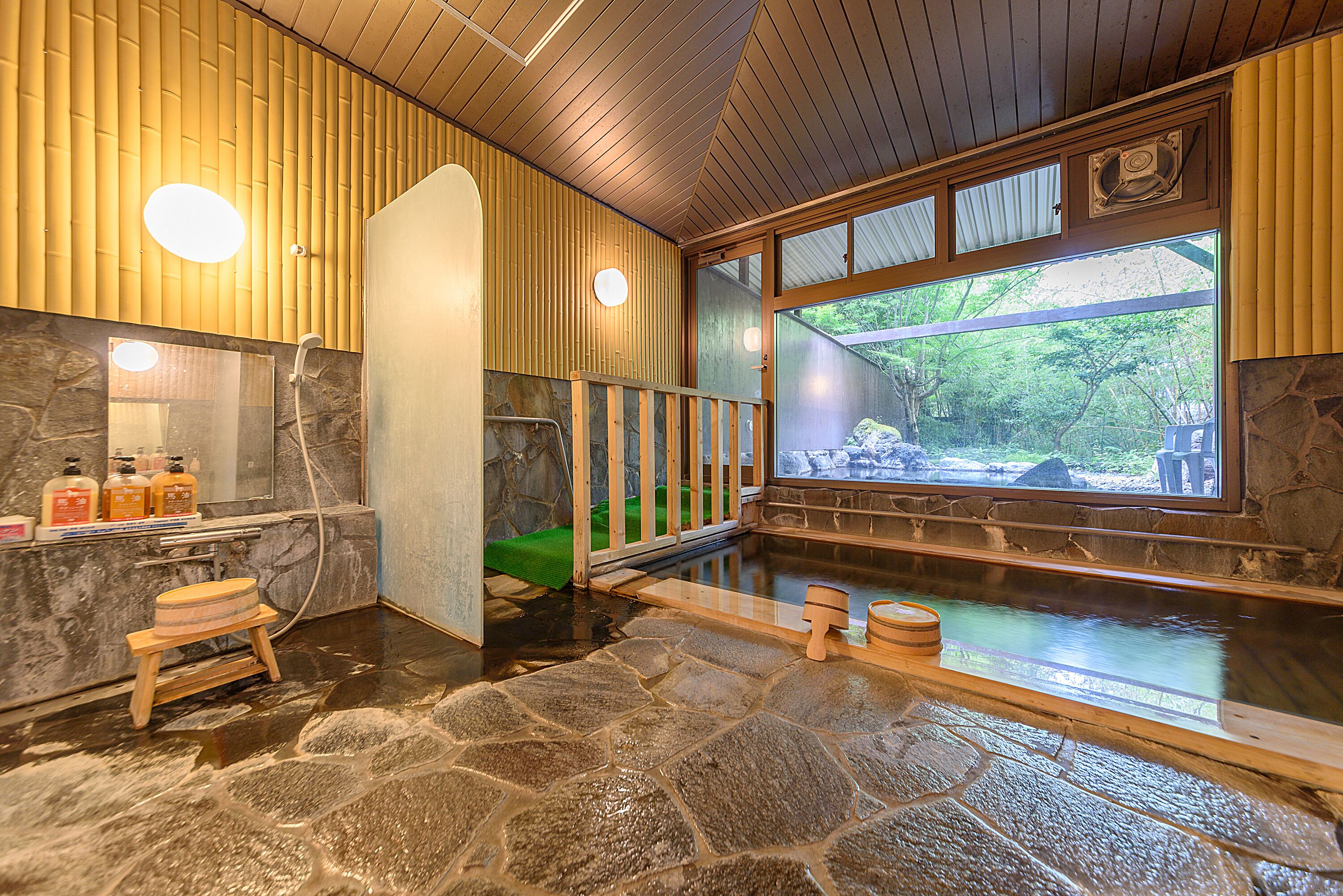 Un onsen japonais traditionnel, avec un sol en pierre, des murs en bois et une vue sur la verdure environnante.