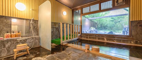 Un onsen japonais traditionnel, avec un sol en pierre, des murs en bois et une vue sur la verdure environnante.
