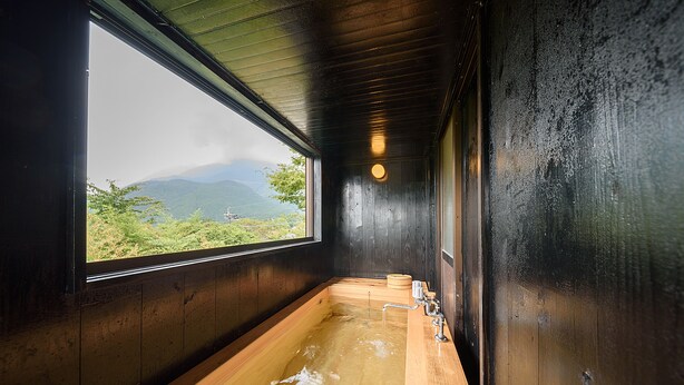 Una bañera de madera con vistas a montañas a través de un ventanal amplio.