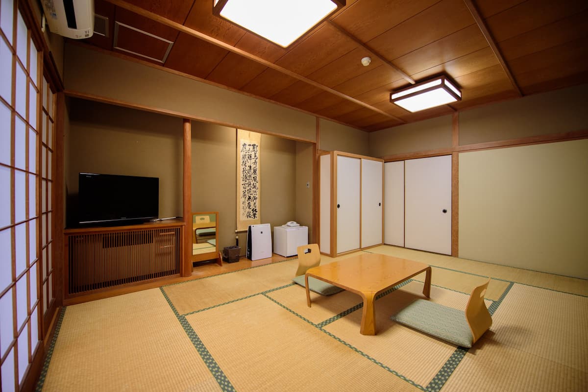 A traditional Japanese room with tatami flooring, a television, a wooden table, and sliding doors.