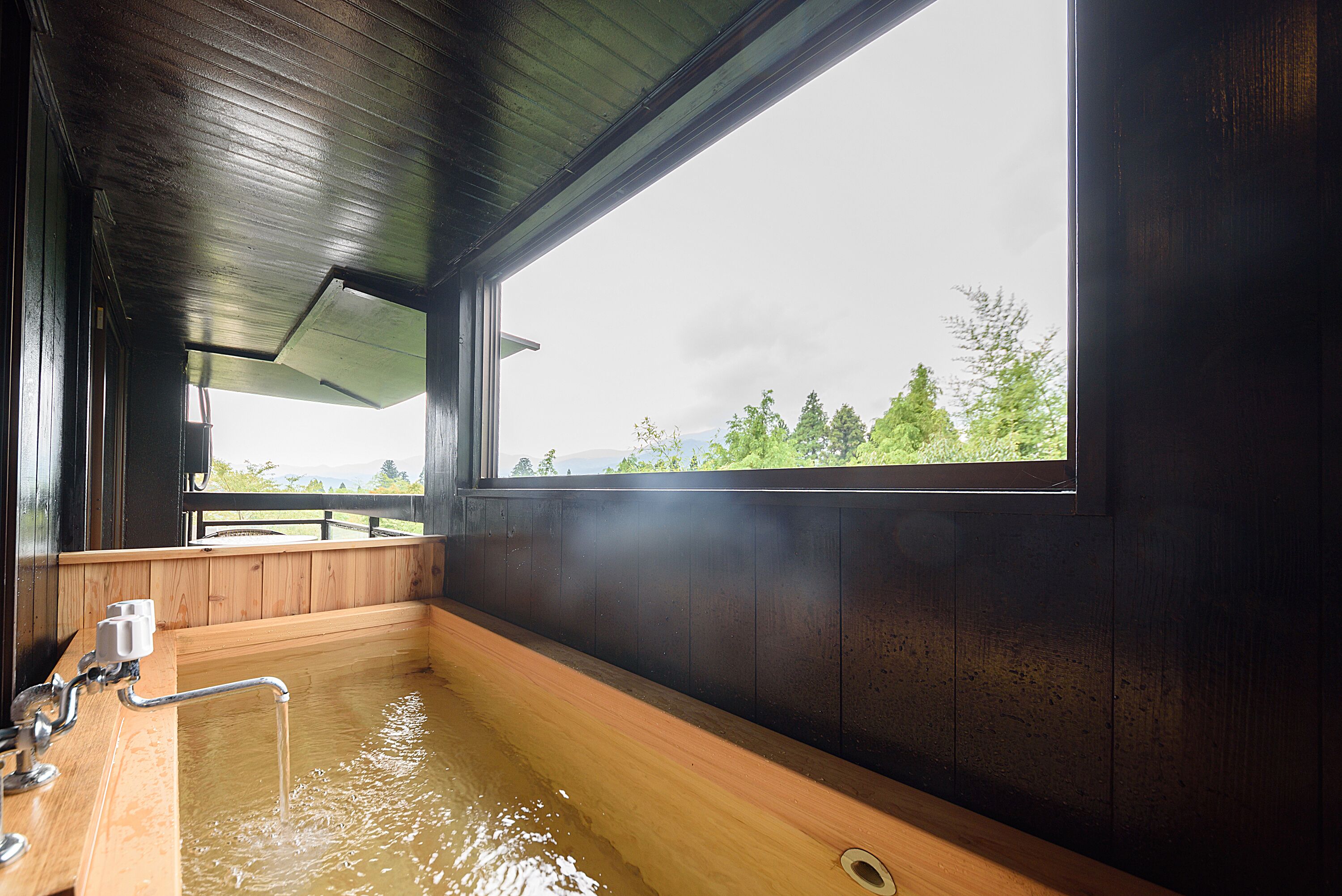 A wooden bathtub with a window, a showerhead, and a faucet.
