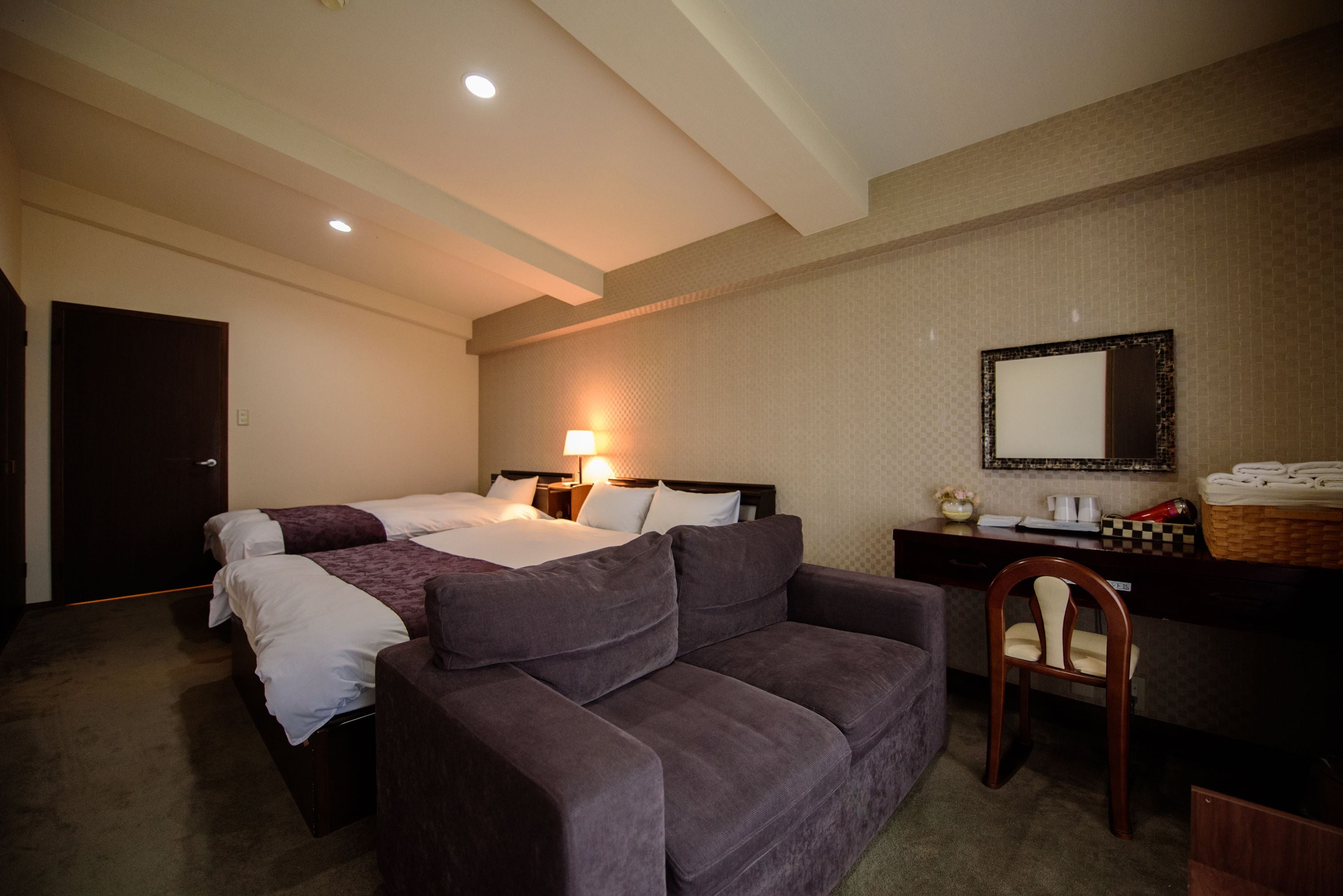 A hotel room with a large bed, a sofa, a desk with a mirror, and a chair.