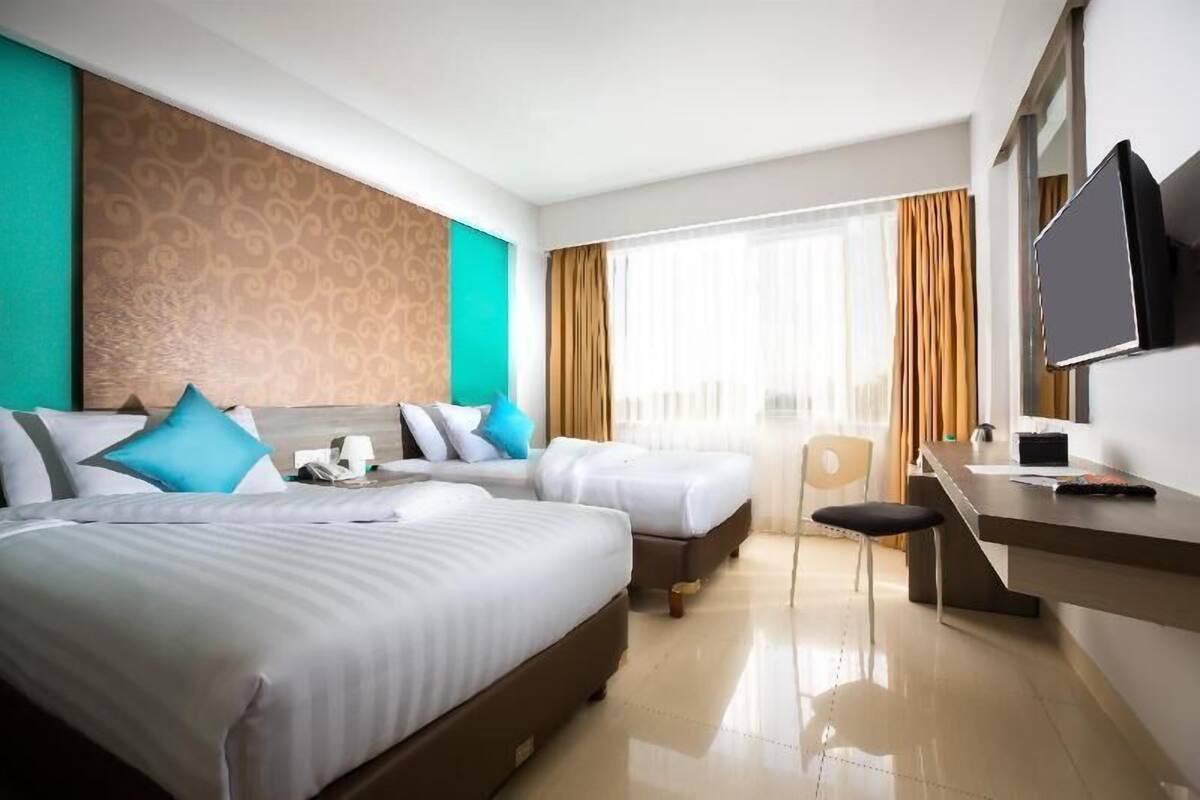A hotel room with two beds, a desk, a chair, a TV, and a window with curtains.