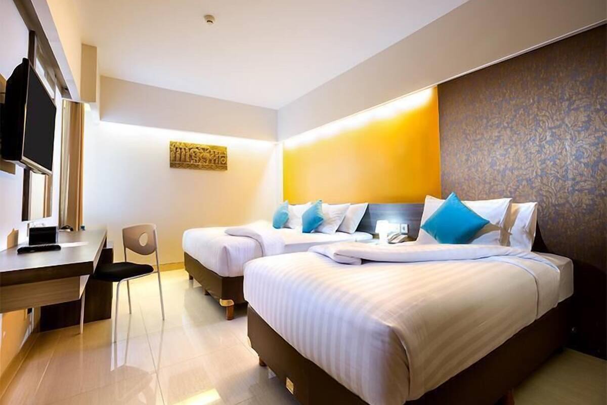 A hotel room with two beds, a desk, a chair, and a television.
