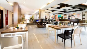 A modern dining area with tables and chairs, a counter with a menu, and a wall with a sign. - Siesta Legian Hotel (Legian)
