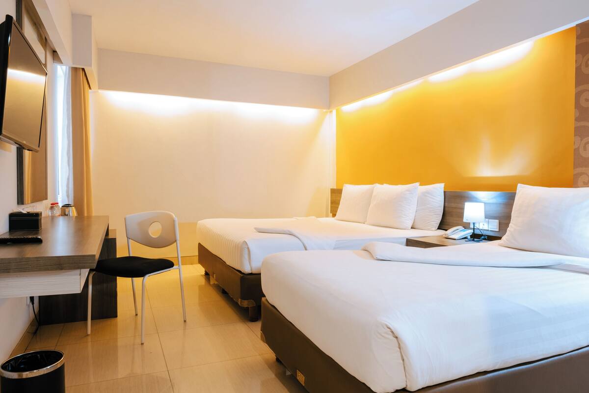 A hotel room with two beds, a desk, a chair, and a TV.