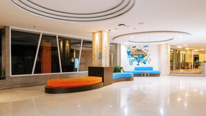 A modern hotel lobby with a large reception desk, seating areas, and a prominent wall mural. - Siesta Legian Hotel (Legian)
