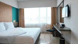 A hotel room with a bed, a desk, a chair, a TV, and a window with curtains. - Siesta Legian Hotel (Legian)