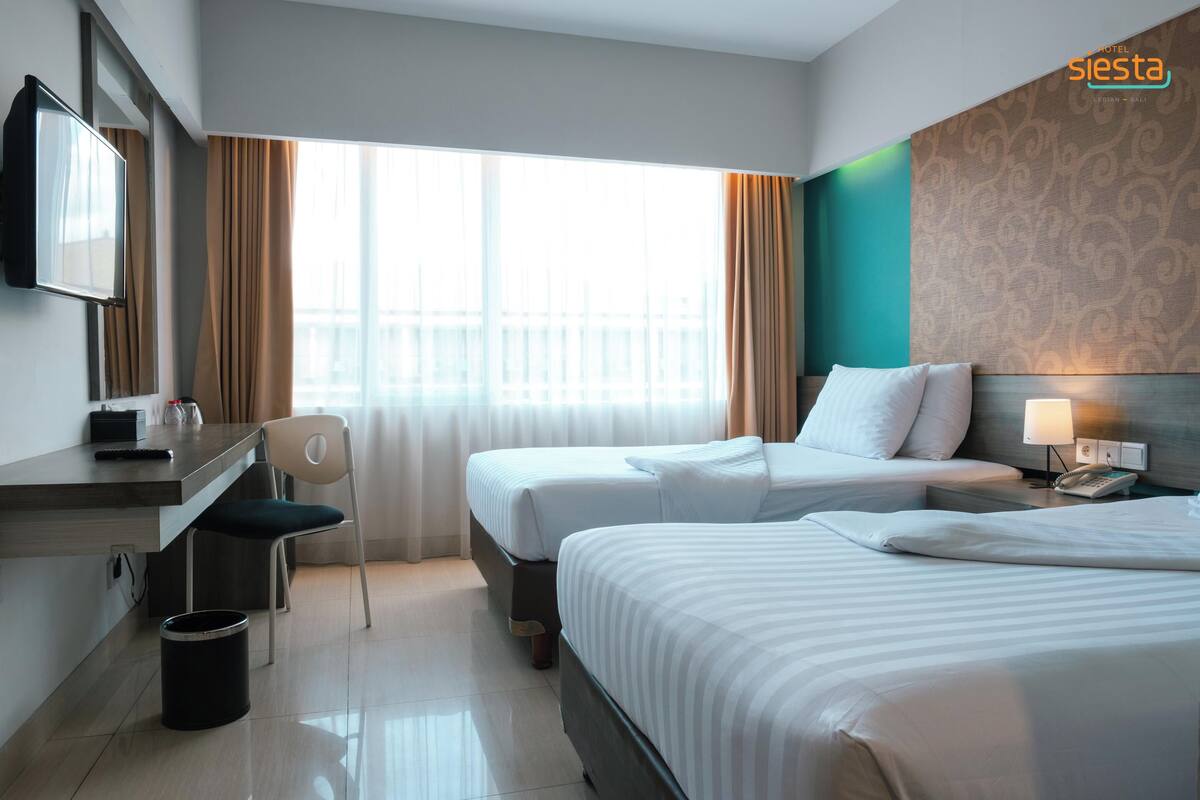A hotel room with two beds, a desk with a chair, a TV, and a window with curtains.
