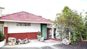 A single-story house with a red-tiled roof, a green door, and a small porch area with a potted plant and rocks. - Millsborough Guest Apartments (Kingston)