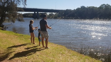 Un hombre y una mujer pescan en un lago tranquilo con un puente al fondo.