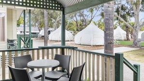 A covered outdoor seating area with tables and chairs, surrounded by trees and white tents in the background. - Central Caravan Park (Ascot)