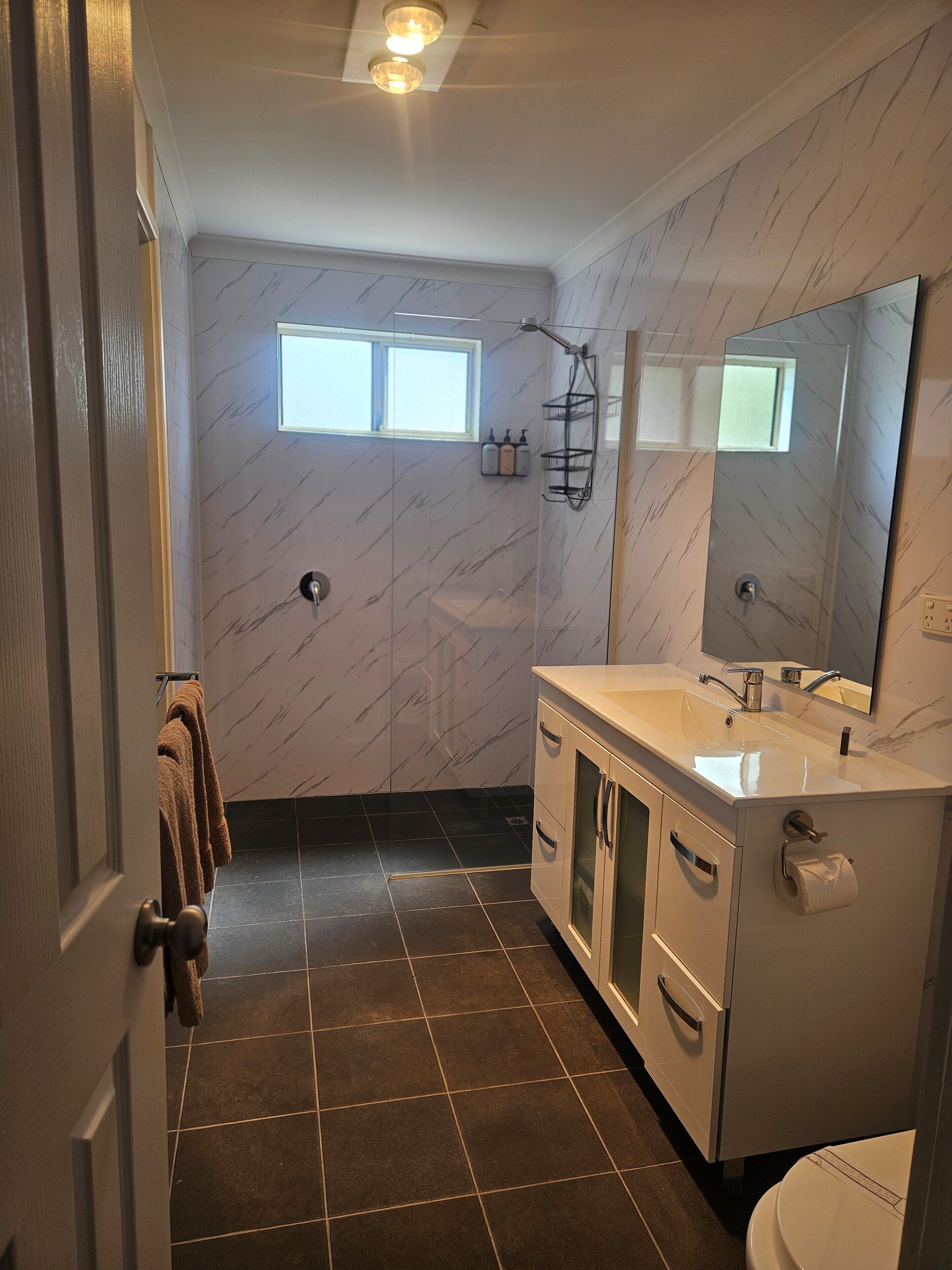 A bathroom with a marble wall, a window, a shower, a sink, and a toilet.