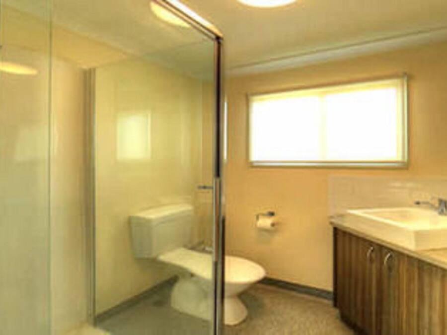 Un baño con cabina de ducha de vidrio, inodoro, lavabo y ventana que proporciona luz natural.