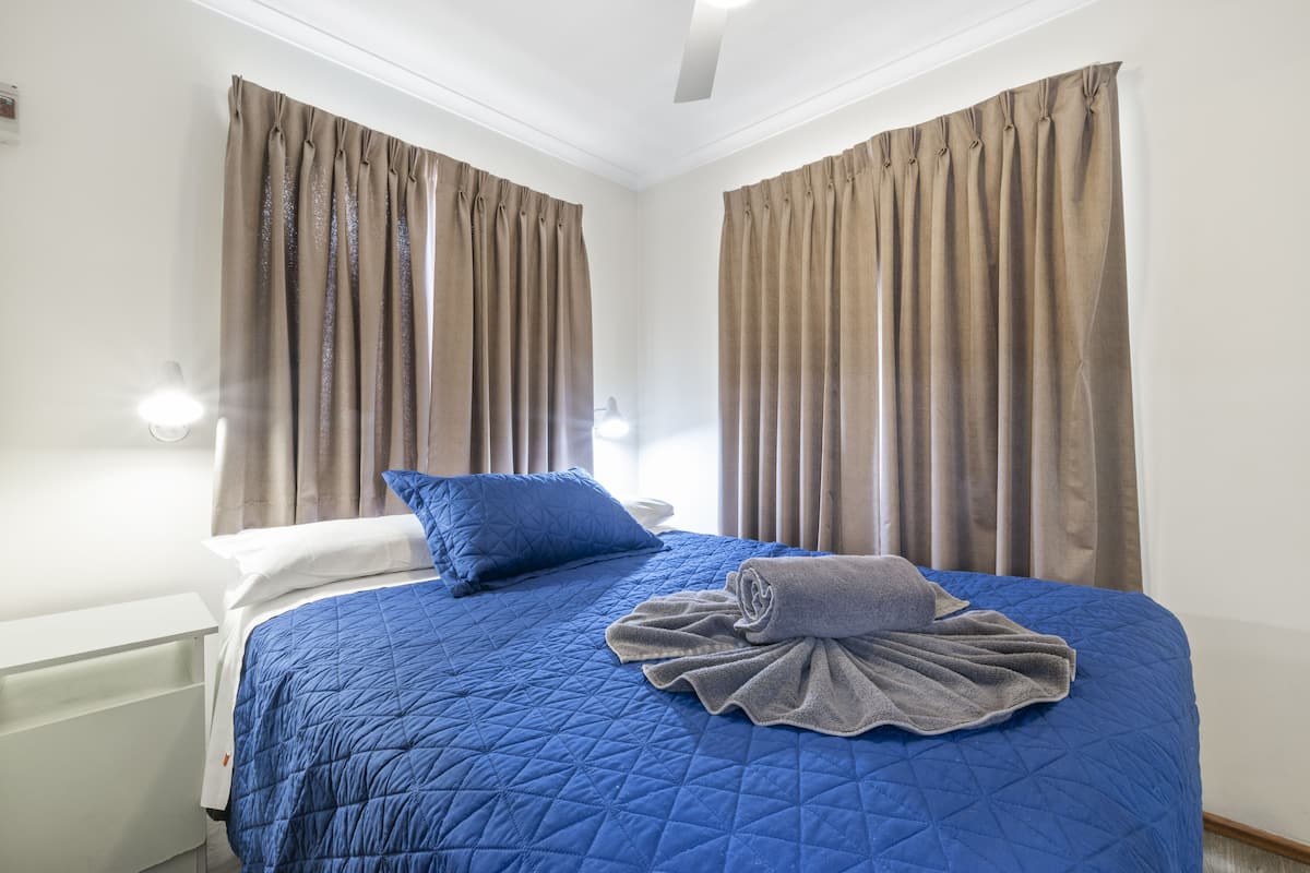 Un lit bien fait, avec une couette bleue, une serviette enroulée et un oreiller bleu.