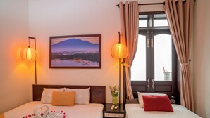 A hotel room with two beds, a nightstand, a lamp, a painting of a landscape, and a window with curtains. - The House 36 (Da Nang)