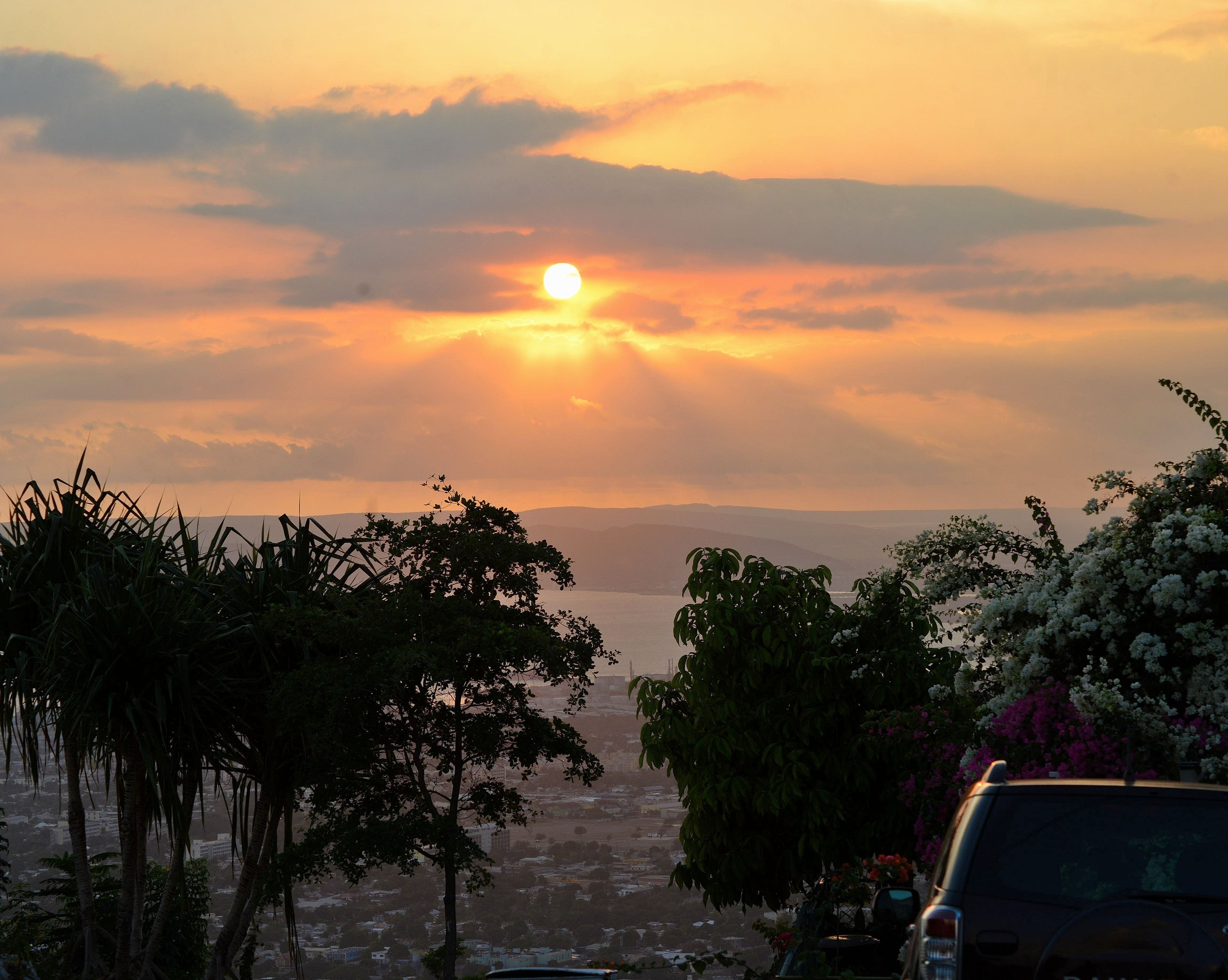 A sunset over a cityscape with visible buildings and trees.