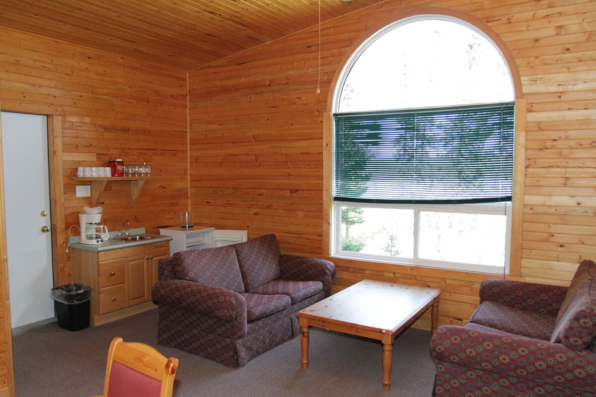 A cozy cabin interior with a wooden interior, a sofa set, a small table, and a window with blinds.