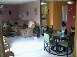 A living room with a beige sofa, a dining table with chairs, and a potted plant.