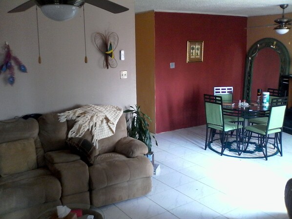 A living room with a sofa, a dining table with chairs, a ceiling fan, and a wall-mounted decorative item. - New Kingston Guest Apartment III (Kingston)