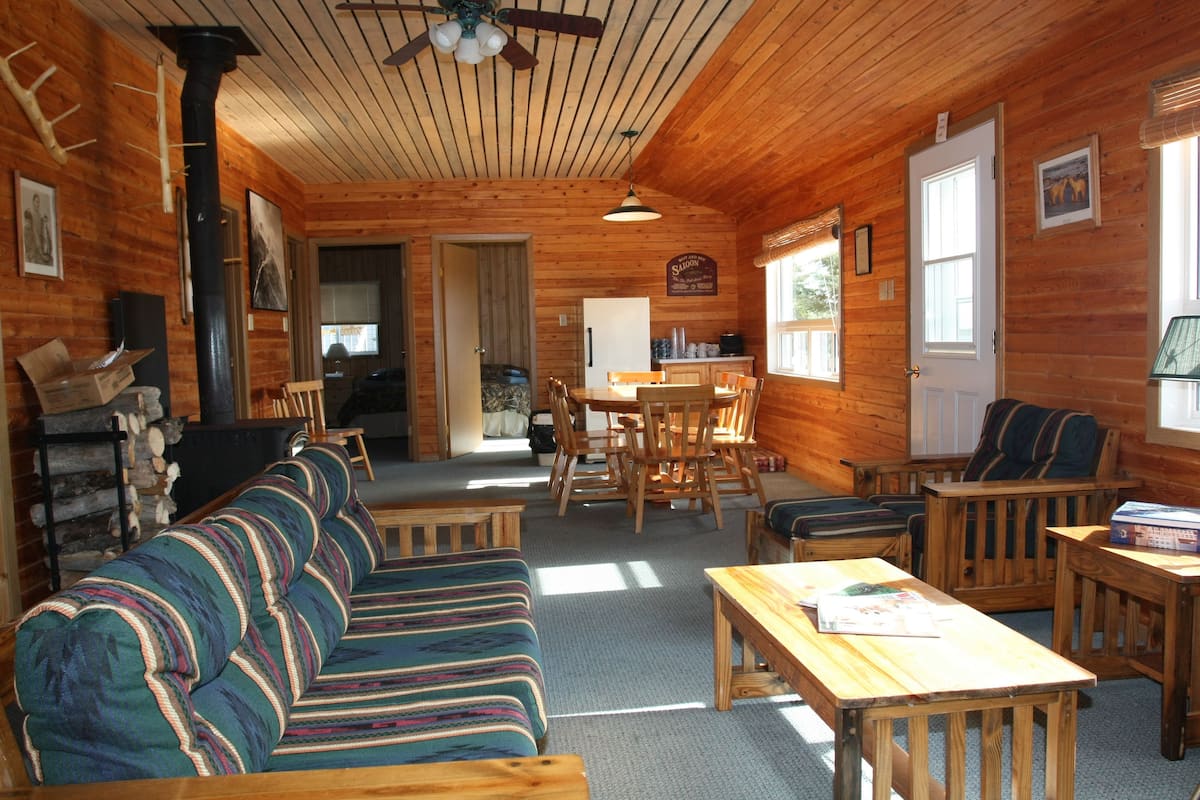 Un interior de cabaña acogedor, con piso de madera, un sofá, una mesa de comedor y sillas.