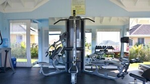 A gym with various exercise equipment, including a squat rack and dumbbells, with a view of houses and greenery outside. - Ocho Rios Ocean View Villa at The Palms (St. Ann's Bay)
