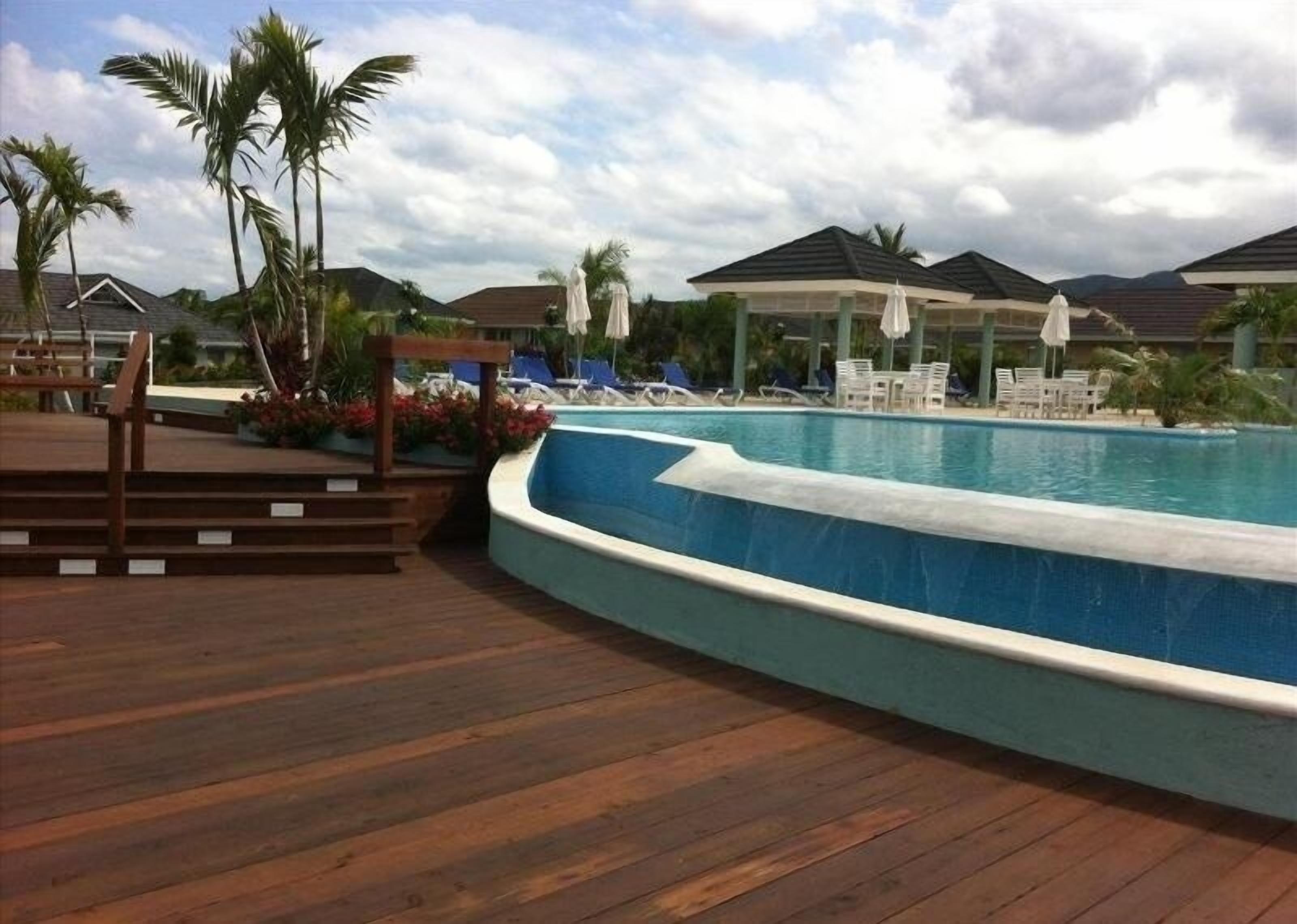 A pool area with wooden decking, lounge chairs, and umbrellas.