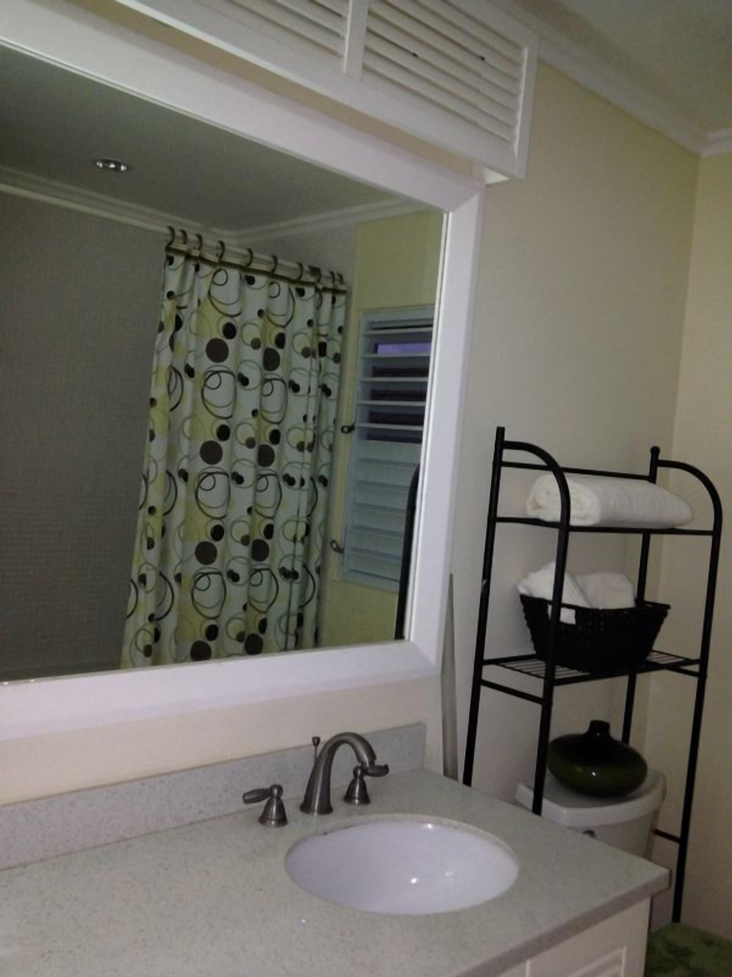 Une salle de bain avec un lavabo blanc, un miroir, un rideau de douche à motifs à pois et une étagère en métal avec des serviettes.
