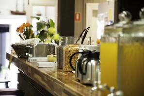A breakfast bar with a coffee pot, cereal containers, and a fruit basket.