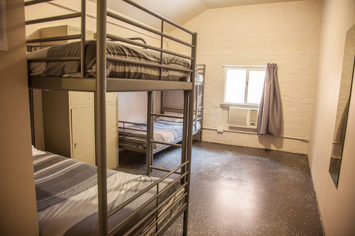 Ein Schlafsaalzimmer mit Etagenbetten, einem Fenster mit Vorhängen und einer Heizung.