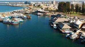 Une vue aérienne d’un port où sont amarrés des bateaux, d’un grand bâtiment doté d’un toit en forme de flèche, et une vue dégagée sur la mer.