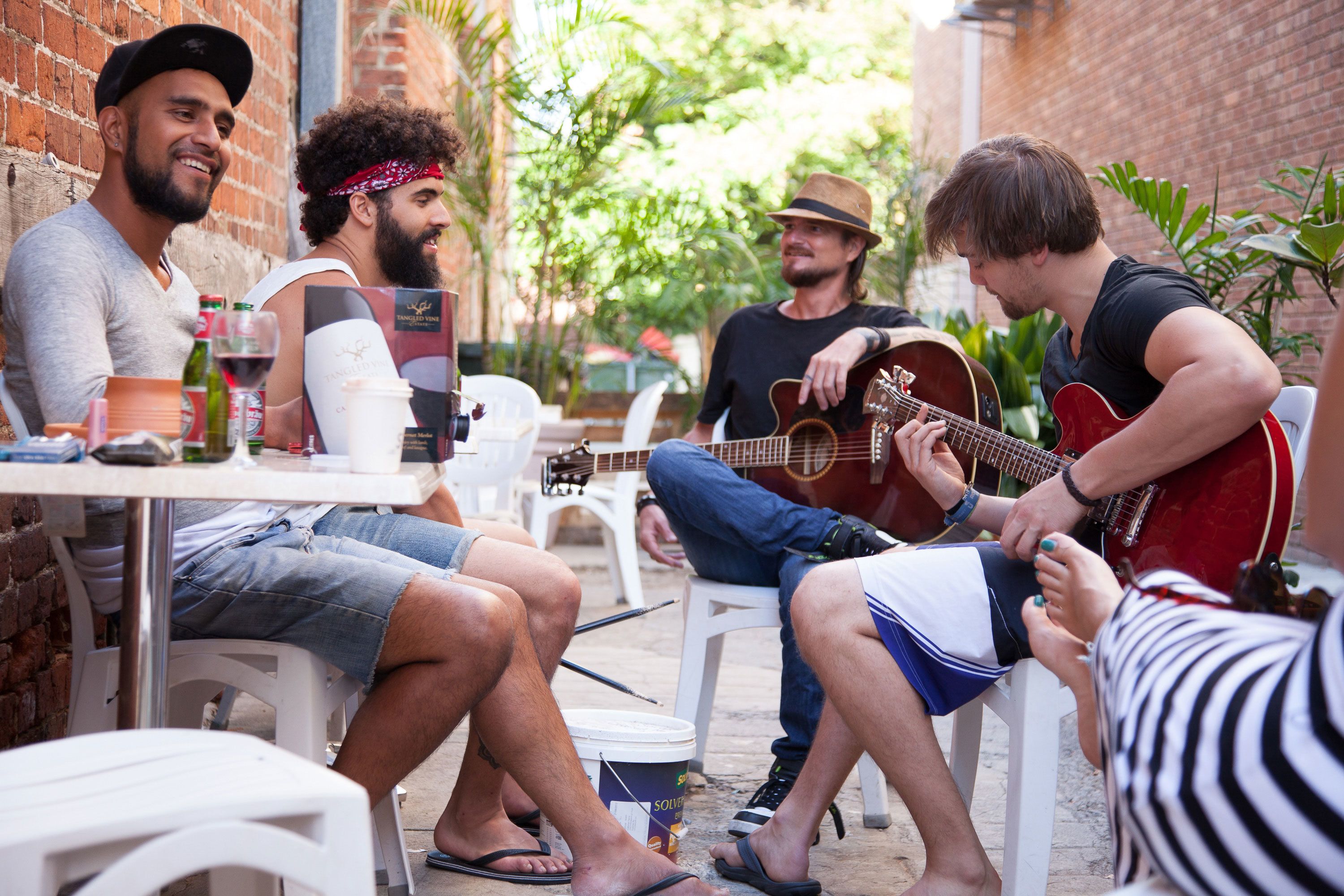 A group of people sitting outdoors at a table with a guitar player performing.