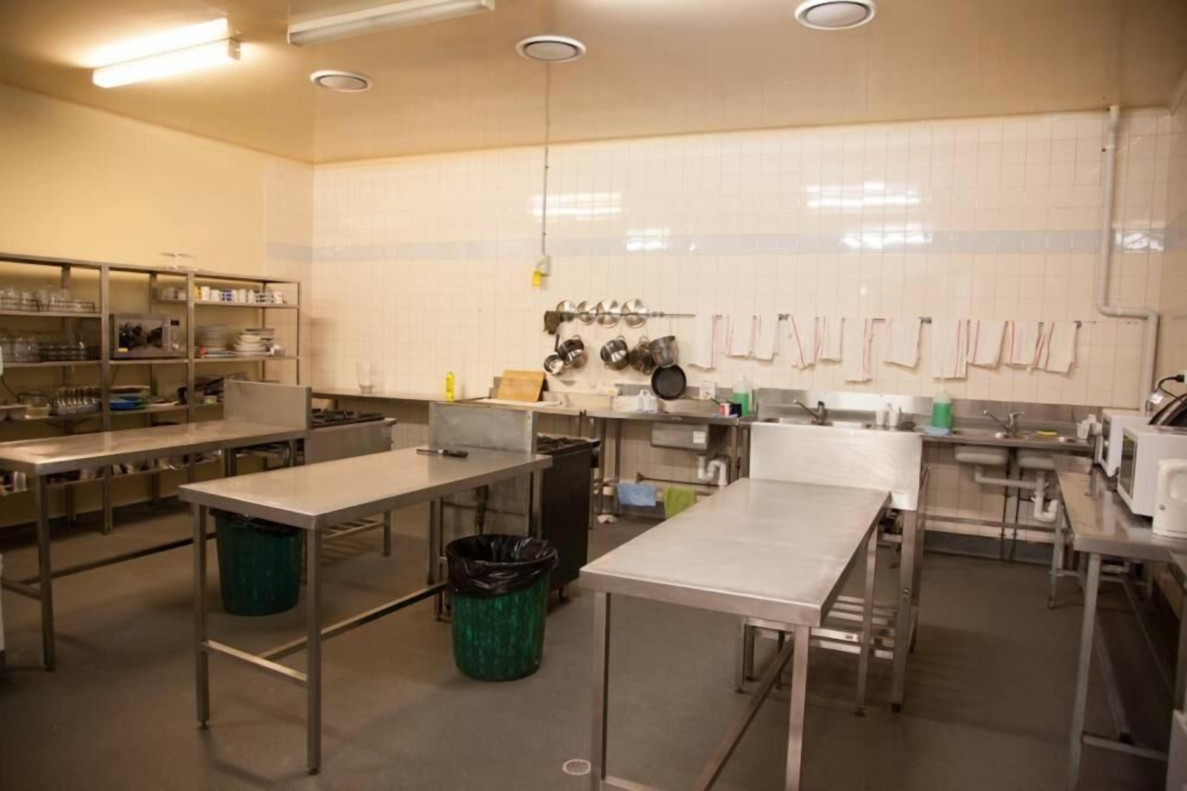 Una cocina amplia con encimeras de acero inoxidable, varios fregaderos y ollas colgantes.