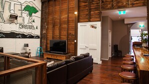 Un espace bar avec un comptoir en bois, des tabourets et un téléviseur posé sur un meuble en bois.