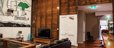 Una zona de bar con barra de madera, taburetes y un televisor sobre un soporte de madera.