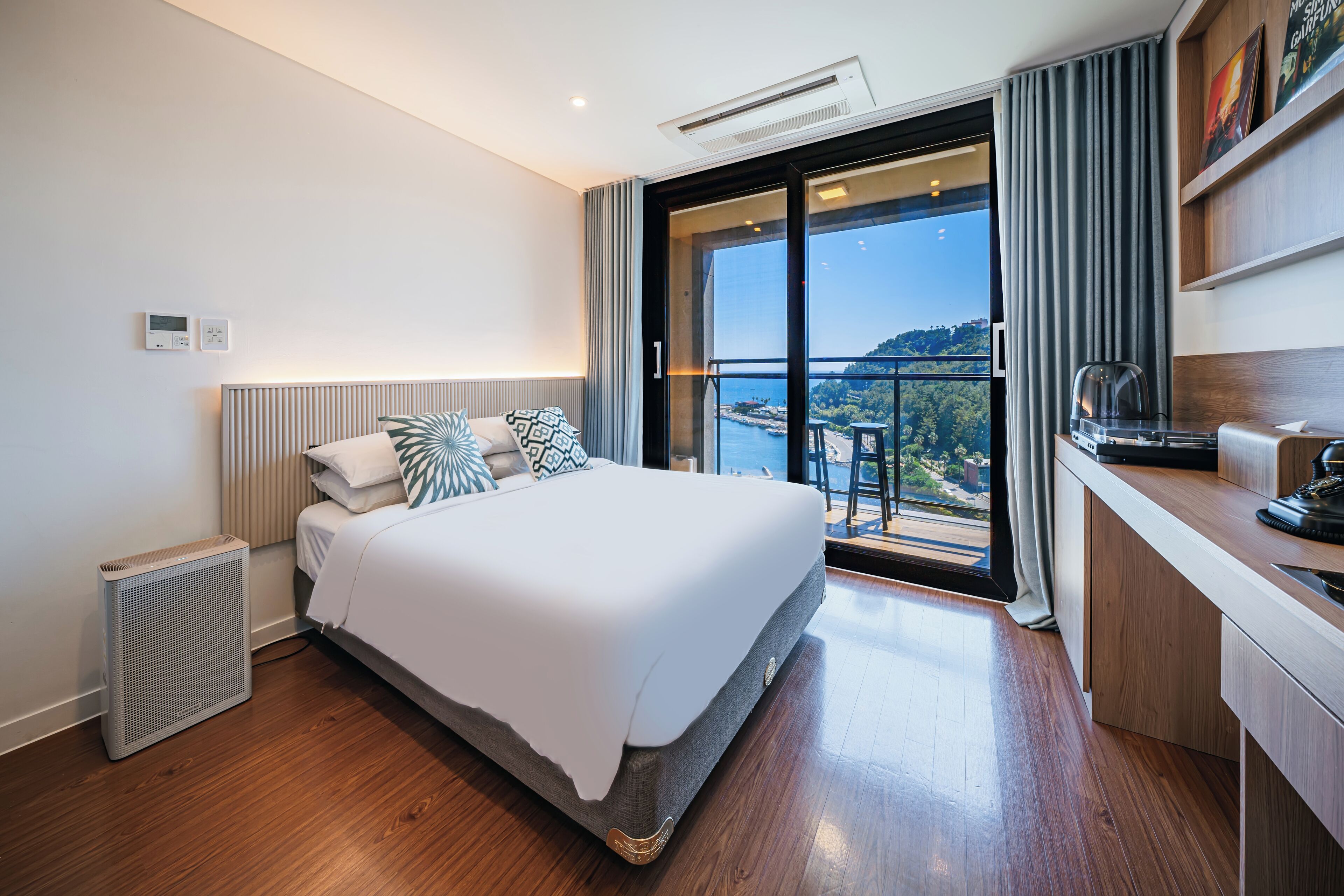 A modern hotel room with a large bed, a desk, and a view of the sea.