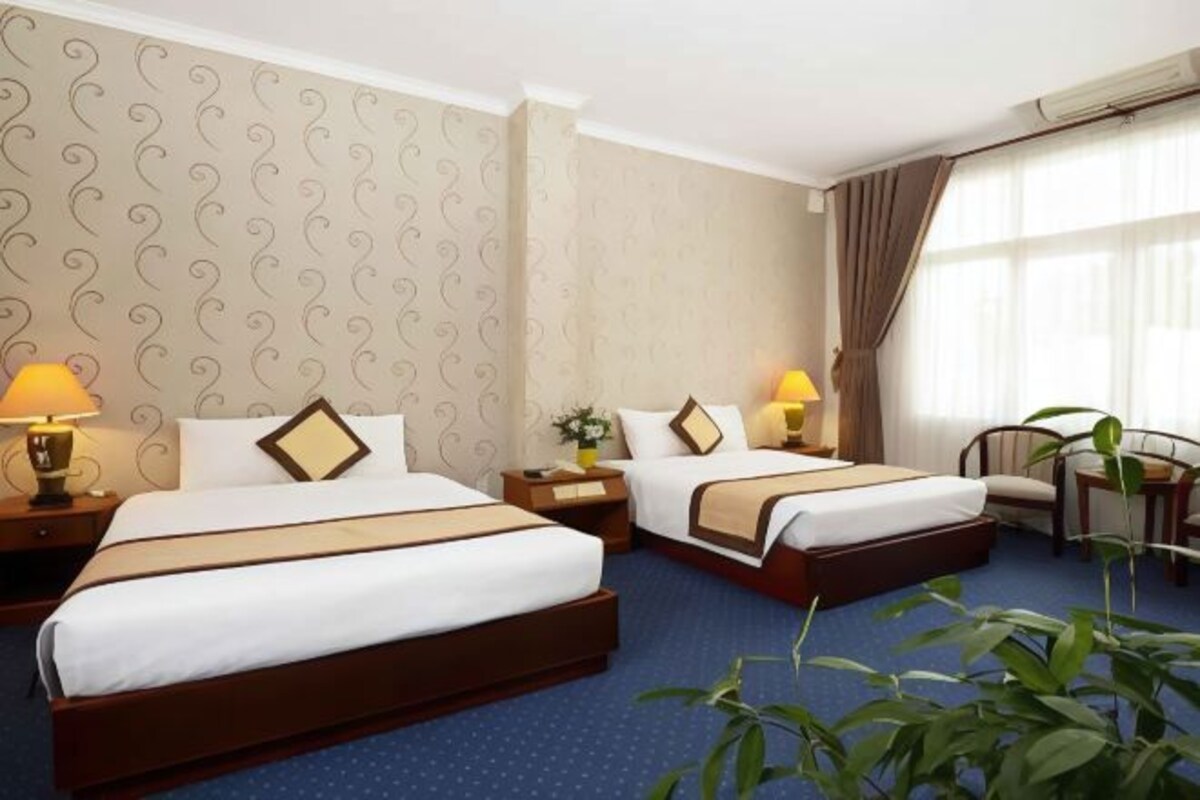A hotel room with two beds, a desk, a chair, and a large window with curtains.